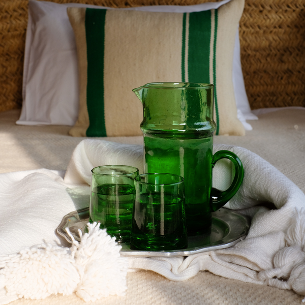Green glass jug on a tray with green glasses on a bed